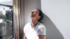 Depressed woman in white shirt leans despairingly against a wall.